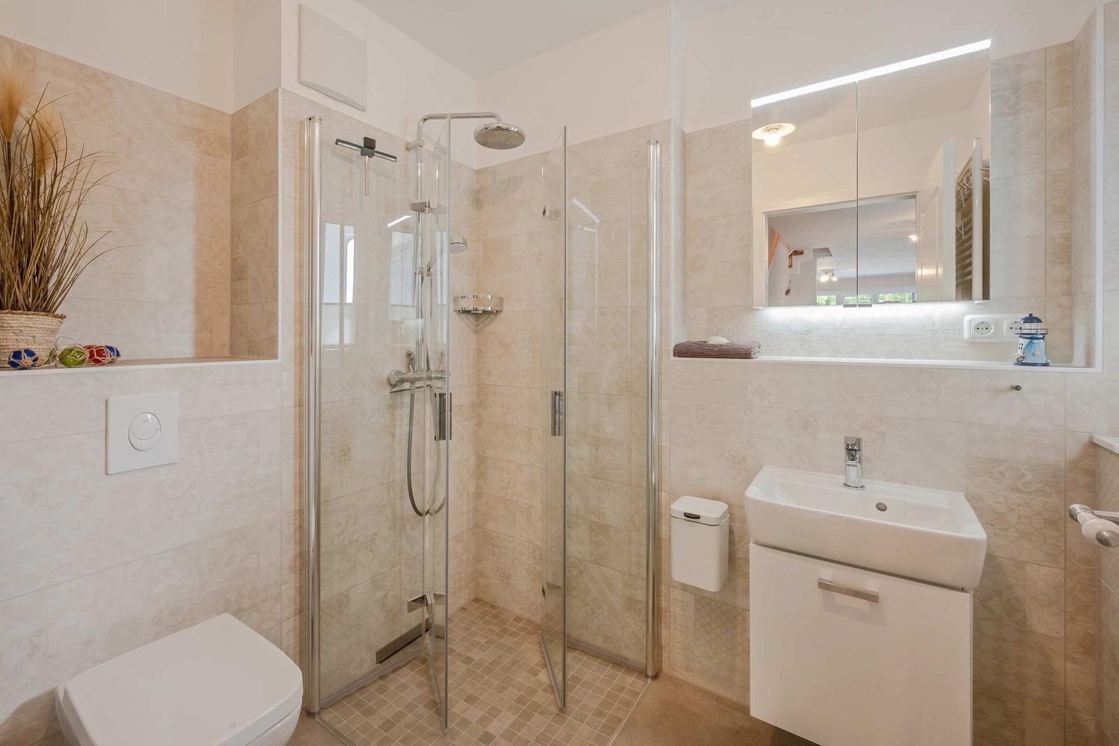 Badezimmer mit Dusche, Waschbecken und Toilette. Fliesenwand und Spiegel.
