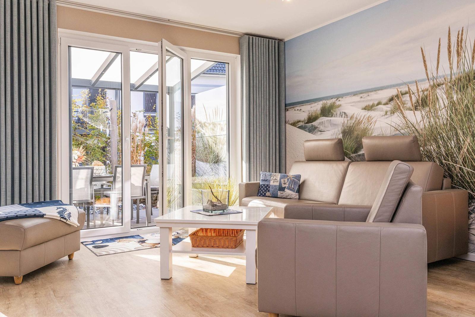 Wohnzimmer mit Sofa, Couchtisch und Terrassentür. Wandbild zeigt Strand.