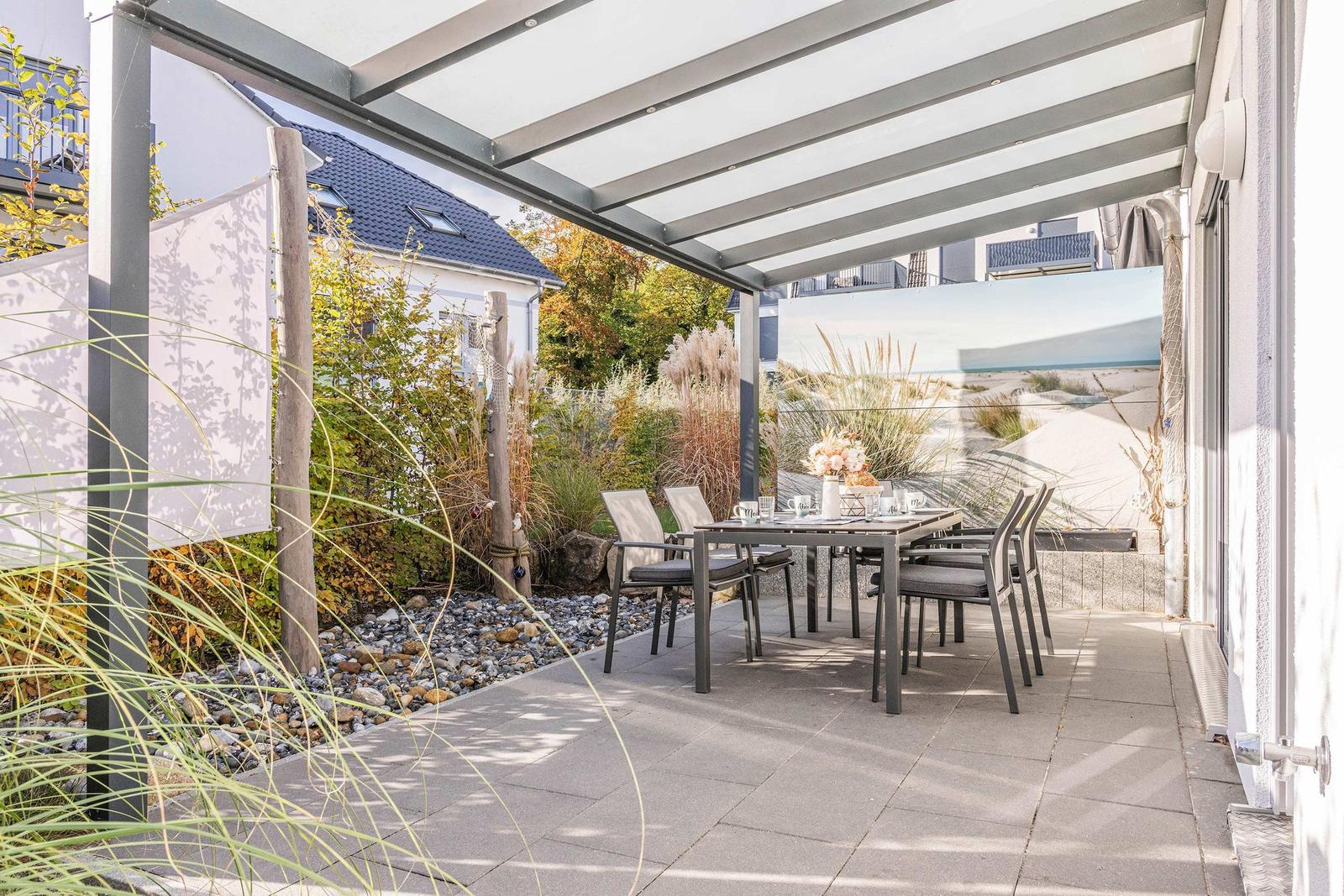 Terrasse mit Sitzgruppe unter Dach, Blick auf Strand und Dünen.