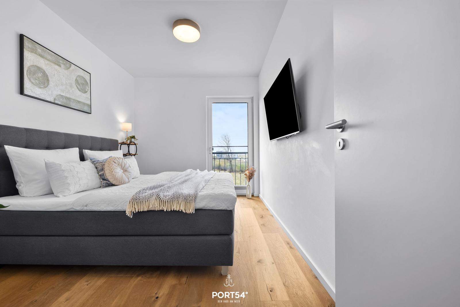Schlafzimmer mit Bett, Fernseher und Balkontür.