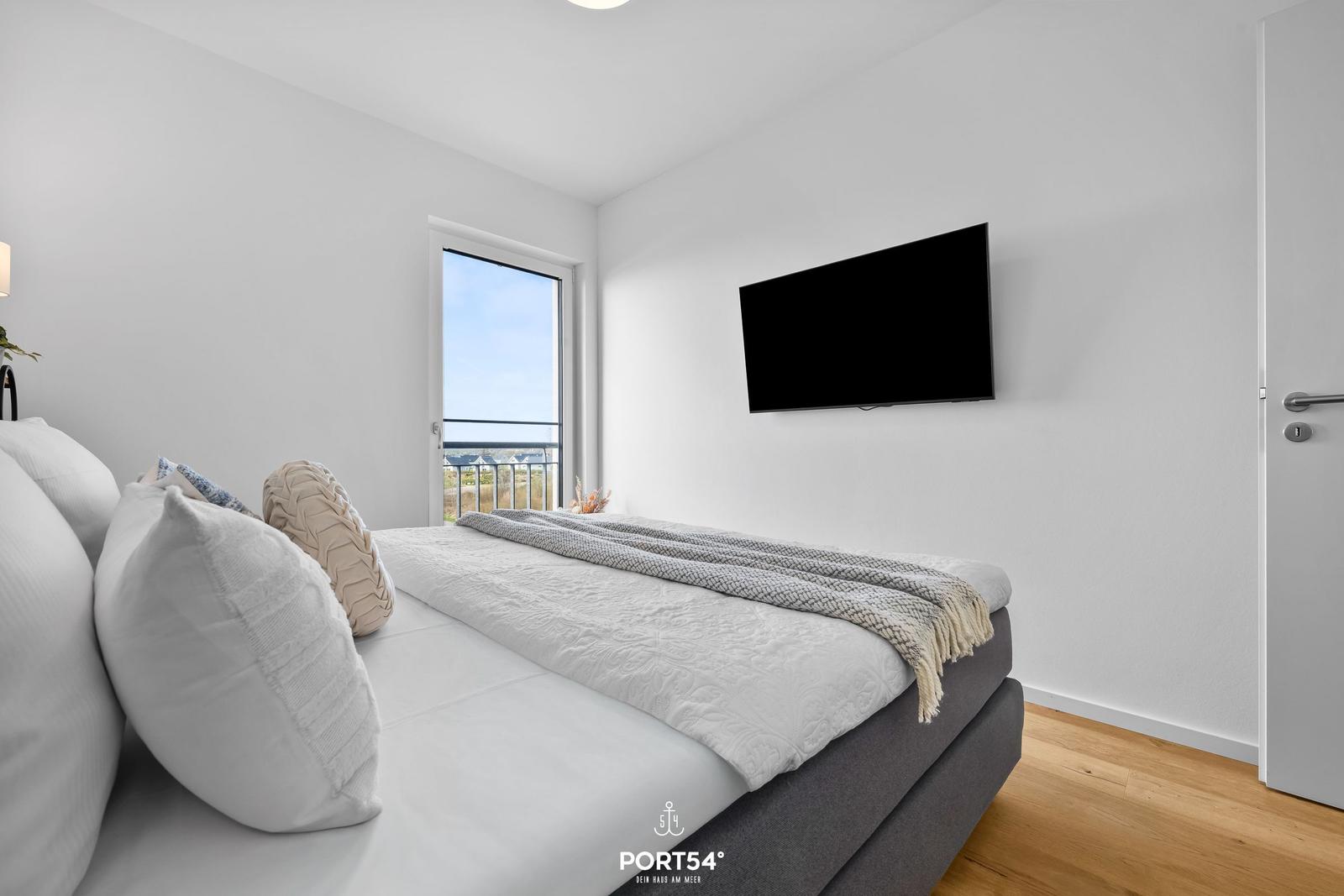 Schlafzimmer mit Bett, TV und Balkontür.