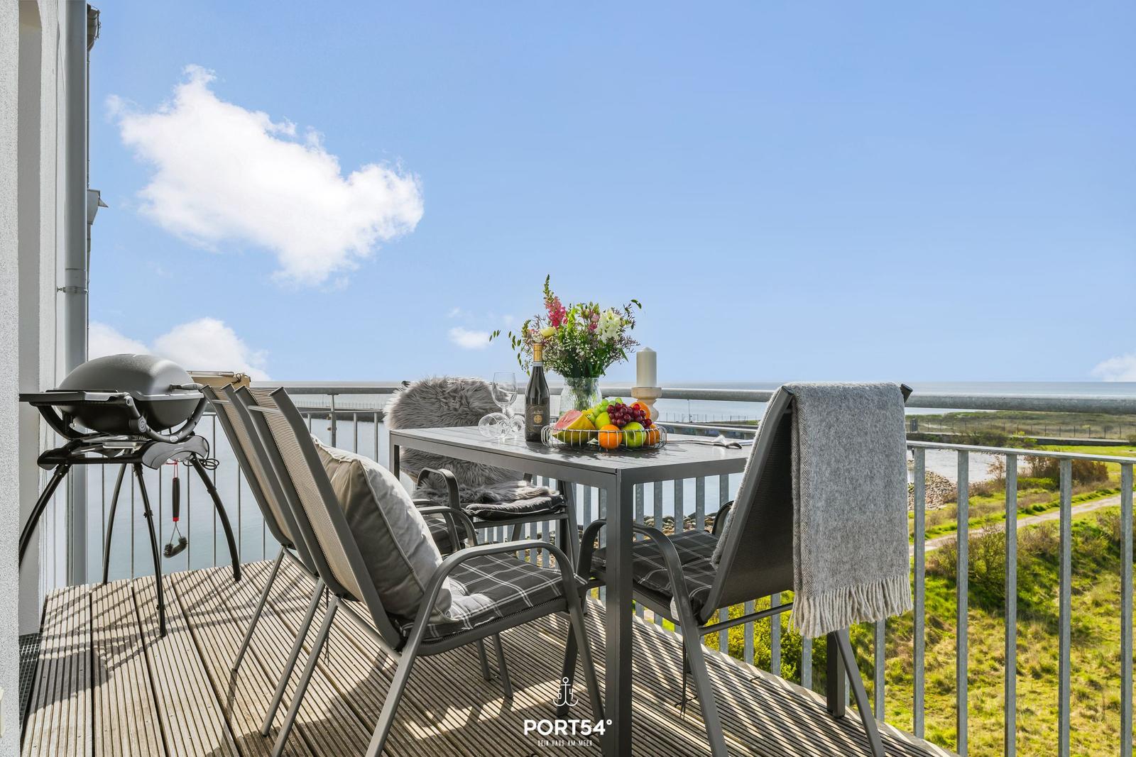 Terrasse mit Tisch, Stühlen, Grill und Meerblick.