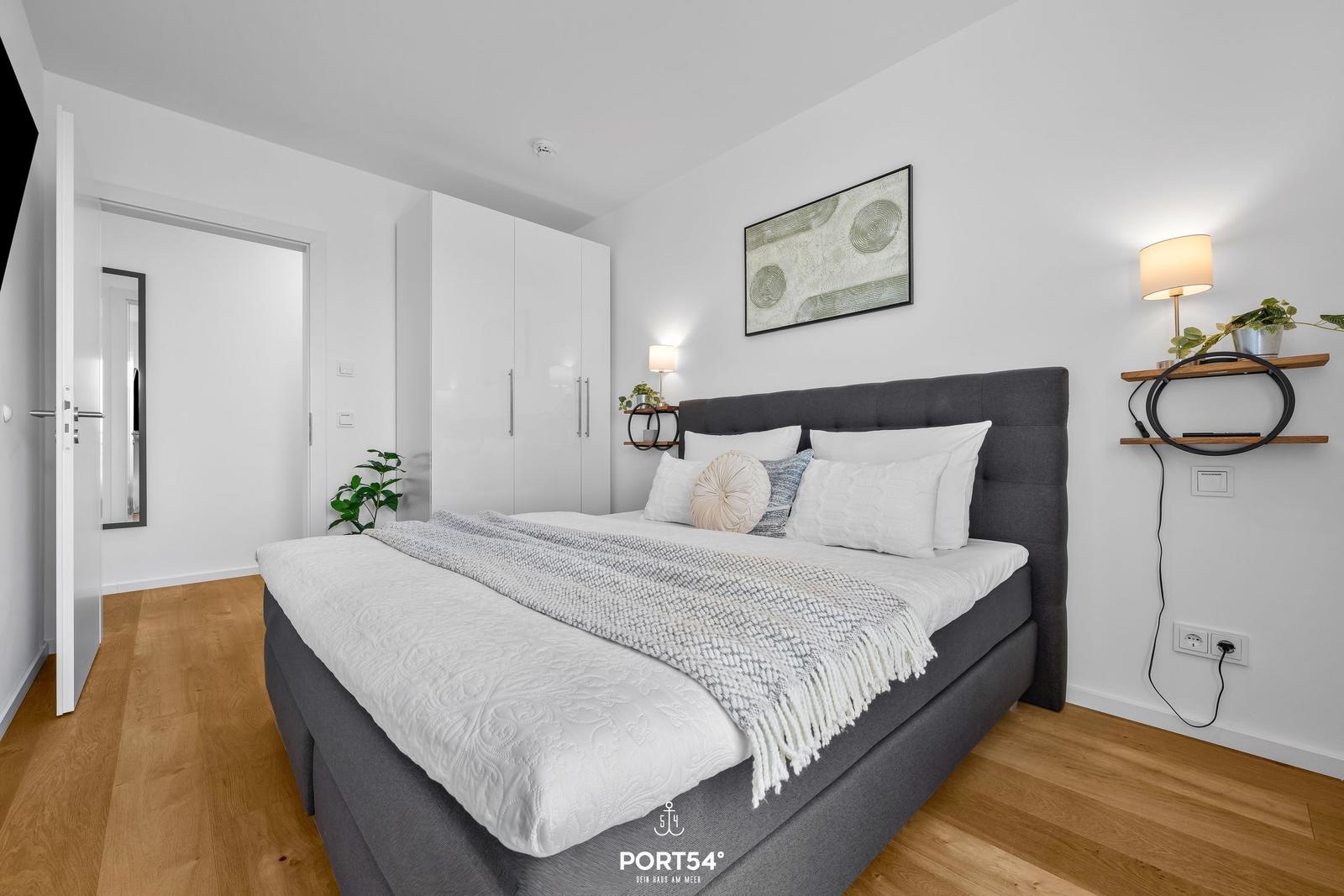 Schlafzimmer mit Bett, Kleiderschrank und Wandbild. Holzboden und Beleuchtung.