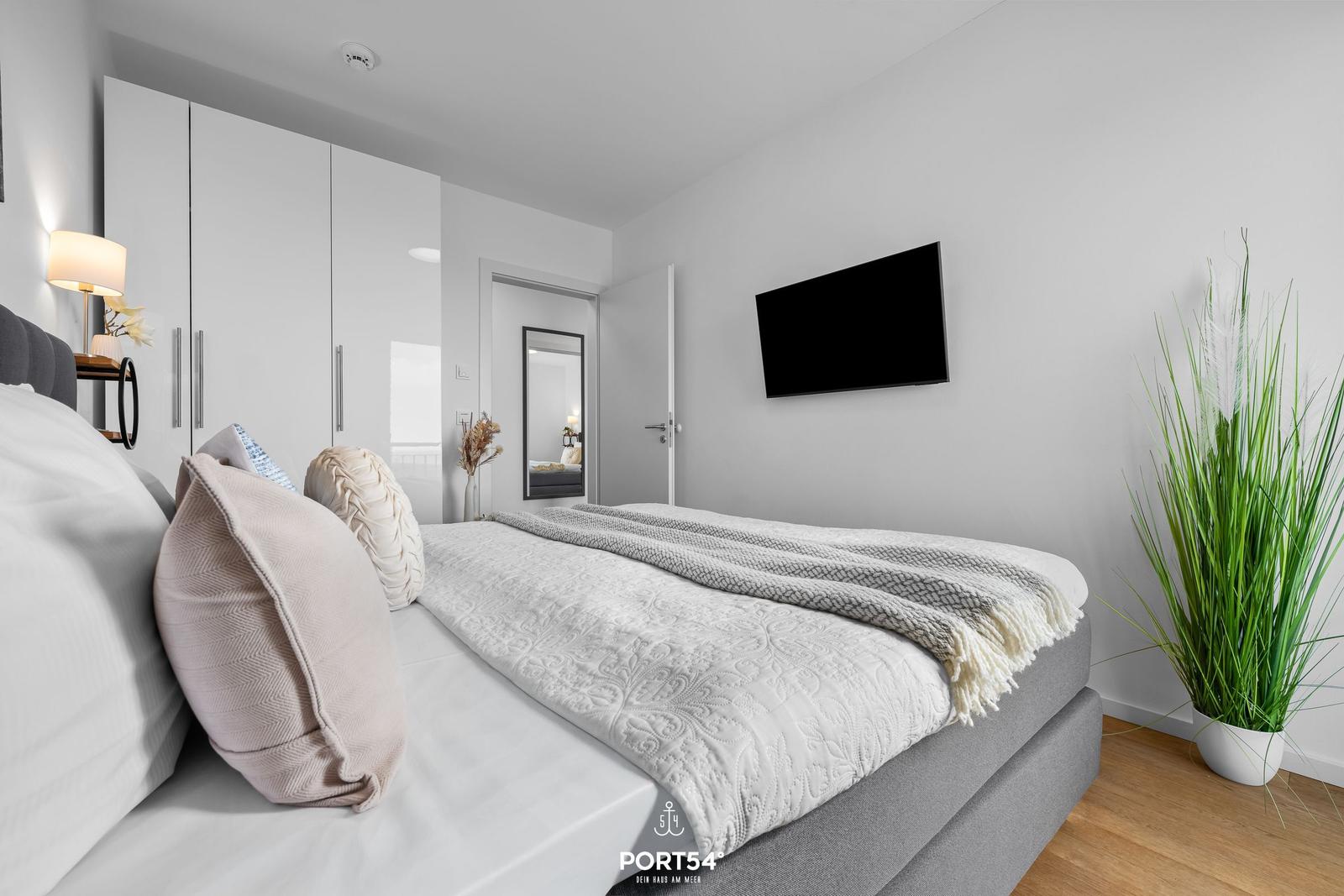 Schlafzimmer mit Bett, Fernseher und Pflanze.