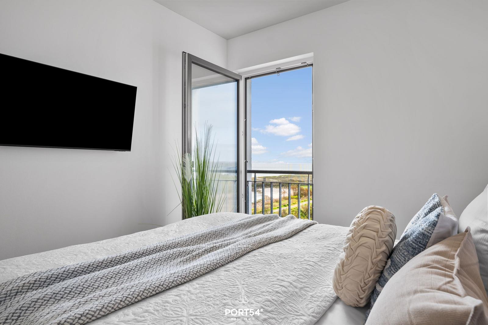 Schlafzimmer mit Blick auf Balkon und Strand. TV an Wand montiert.