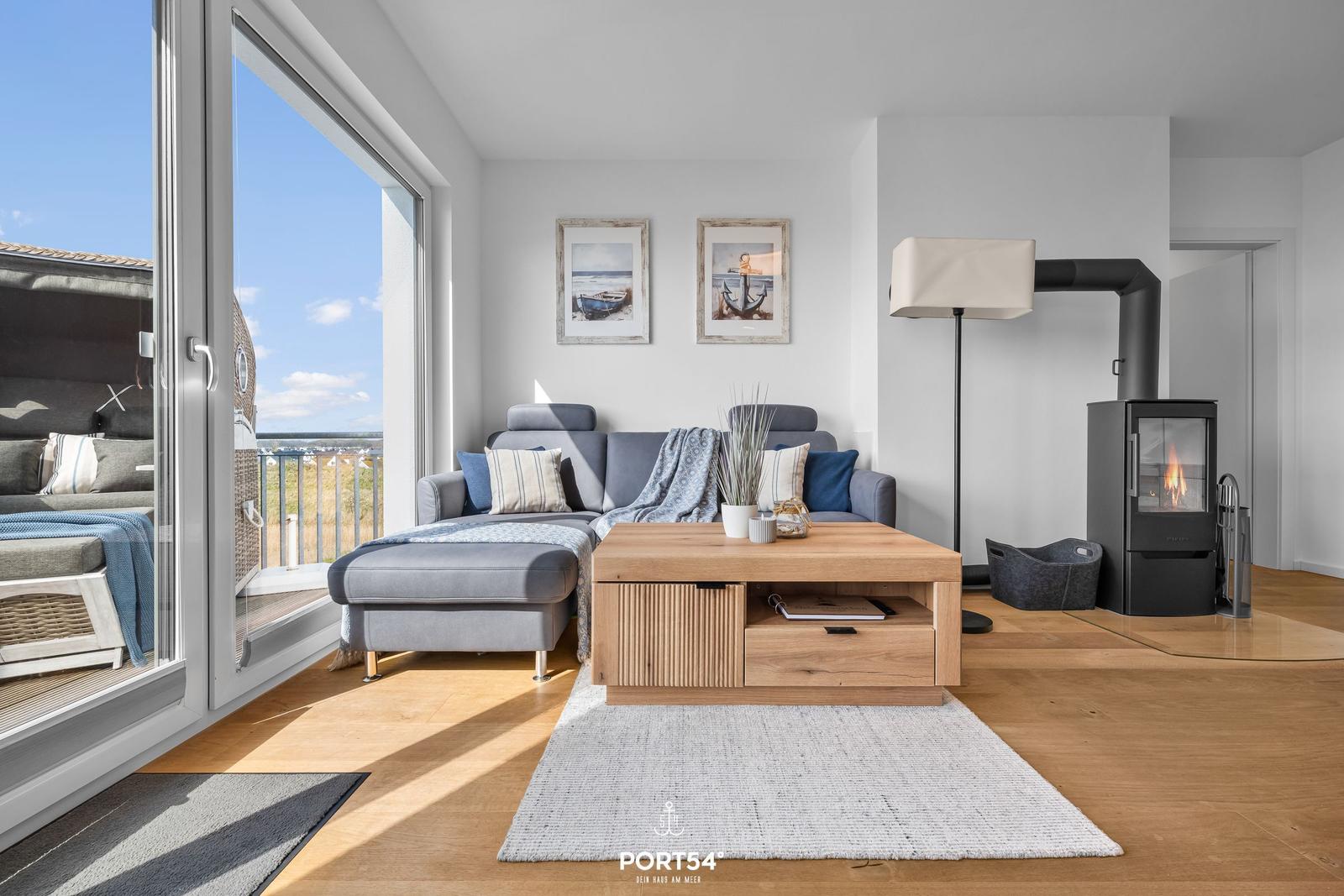 Wohnzimmer mit Sofa, Kamin und großem Fensterblick auf den Strand.