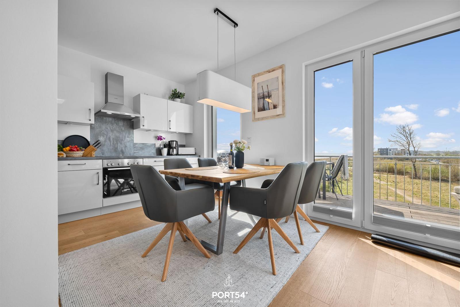 Essbereich mit Tisch und Stühlen, Küche und Balkon mit Blick auf Grünfläche.