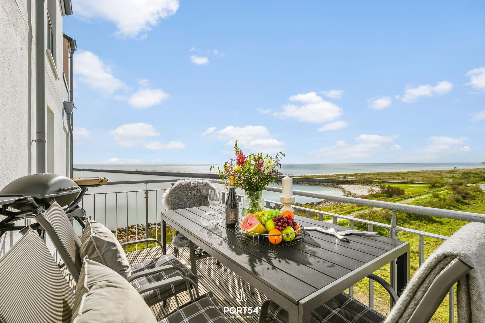 Terrasse mit Tisch, Stühlen und Grill. Blick aufs Meer und grüne Landschaft.