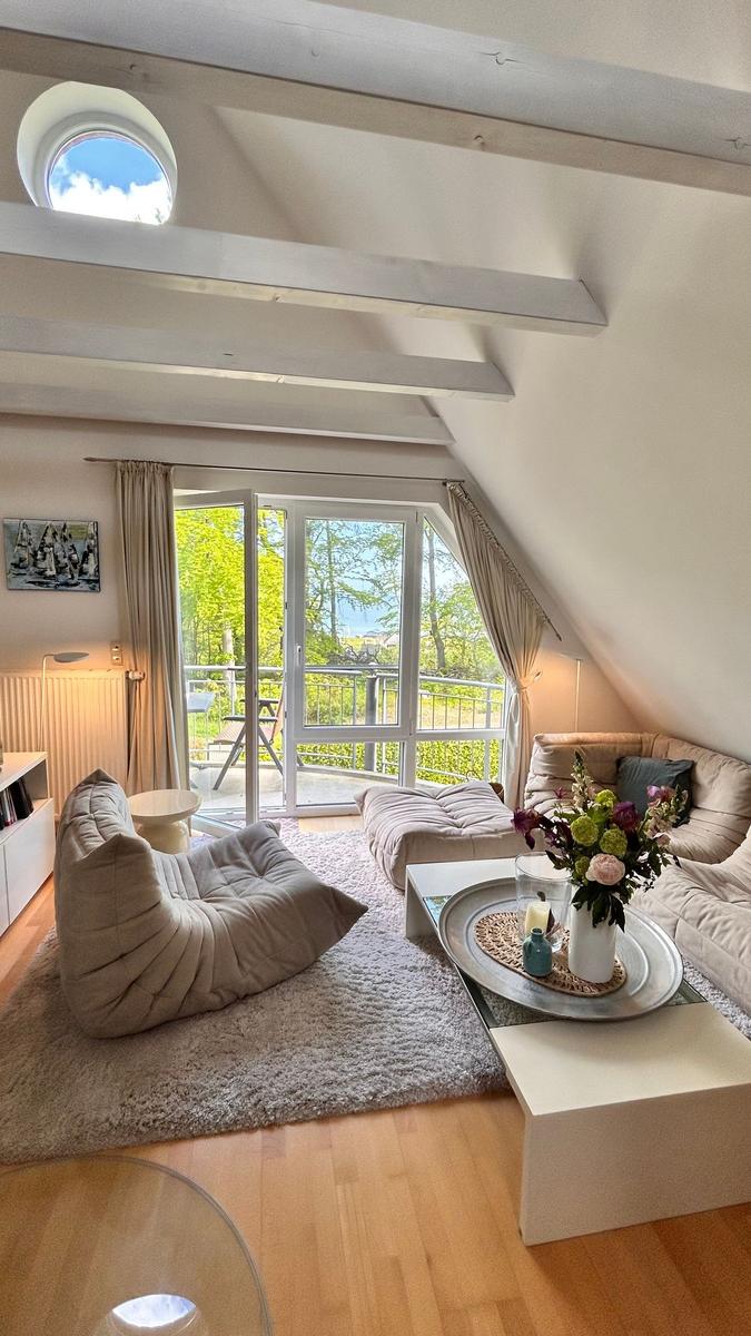 Wohnzimmer mit Sitzgelegenheiten, Glasfront und Dachfenster. Holzboden und helles Interieur.