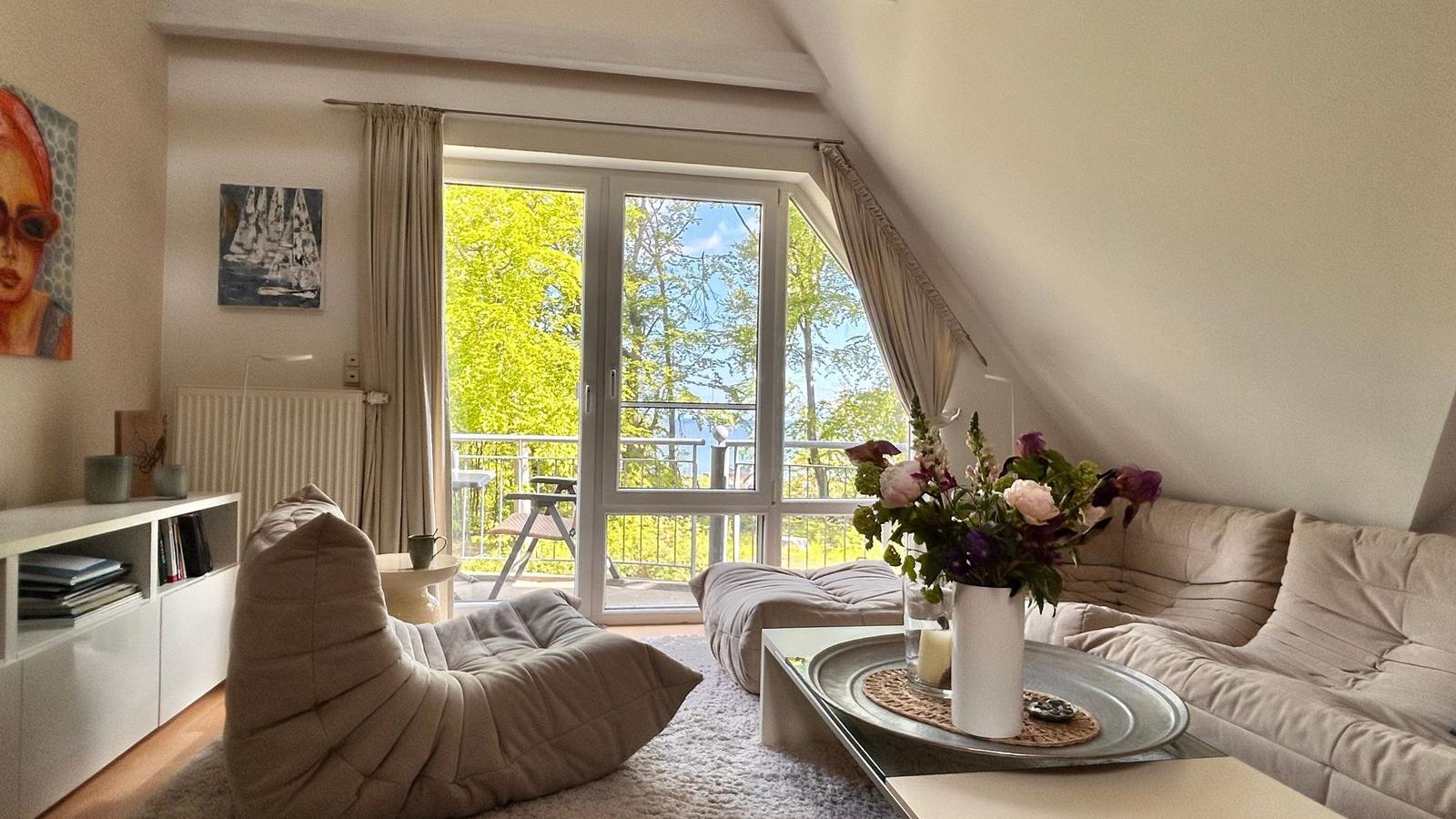 Wohnzimmer mit Schlafsofa, Couchtisch und Balkon. Blick auf grüne Bäume.