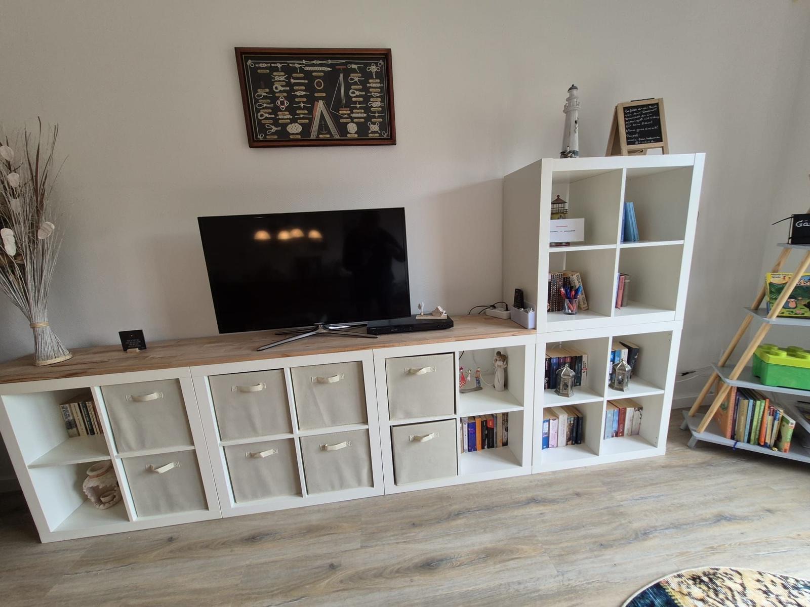 TV auf Holzregal mit Aufbewahrungsboxen und Bücherregal daneben.