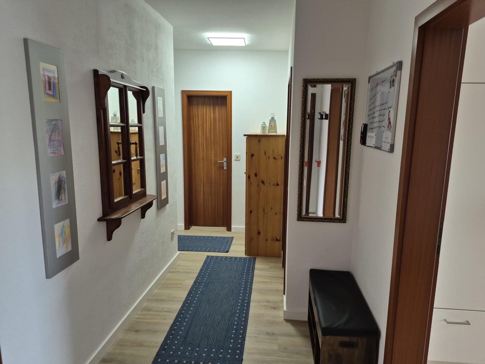 Flur mit Holzboden, blauem Teppich, Spiegel und Garderobe.