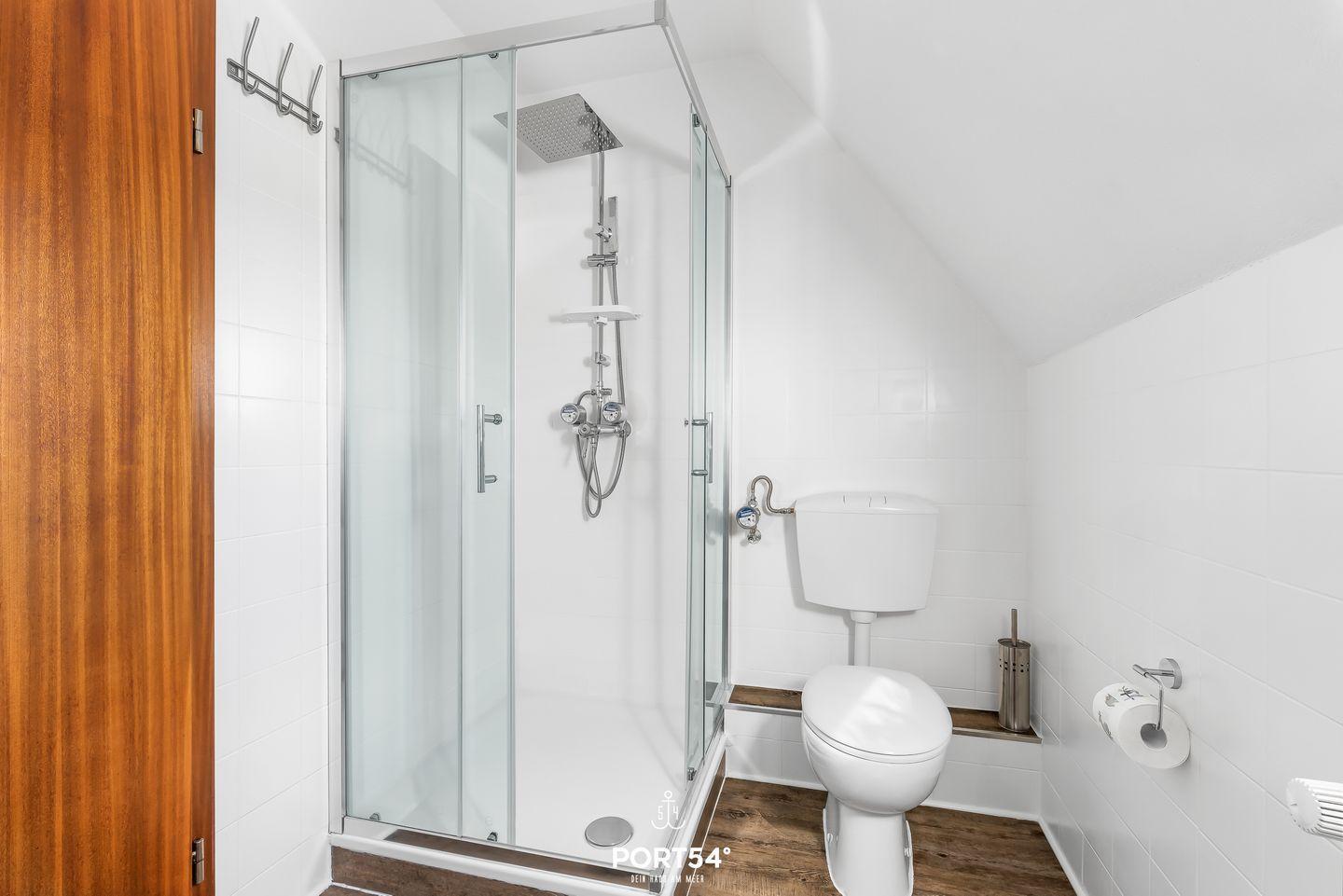 Duschkabine mit Duschbrause, Toilette und Holzboden