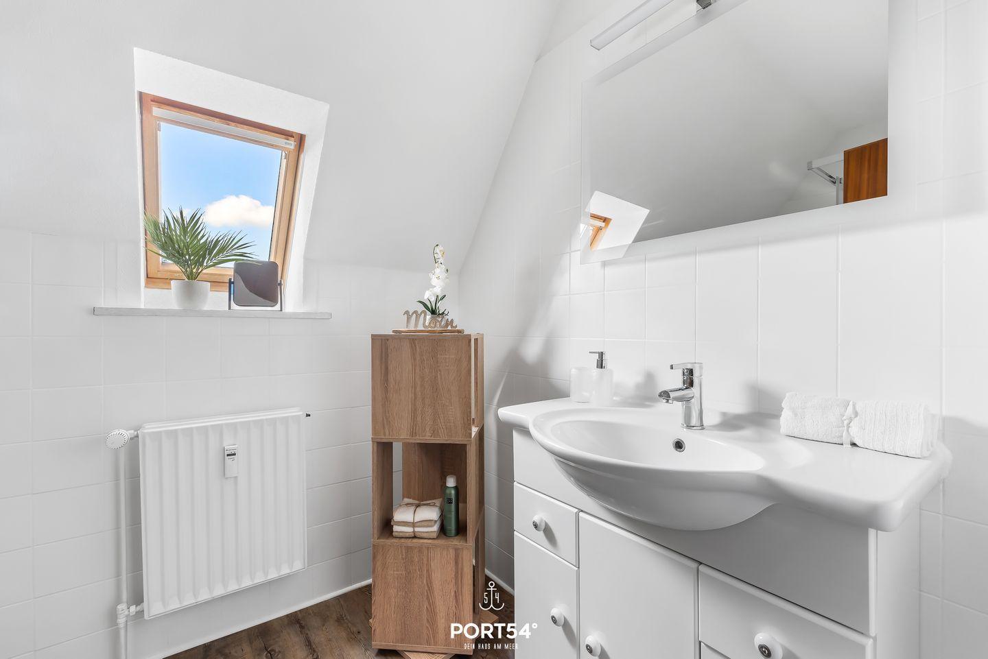 Badezimmer mit Waschbecken, Spiegel, Dachfenster und Holzregal.