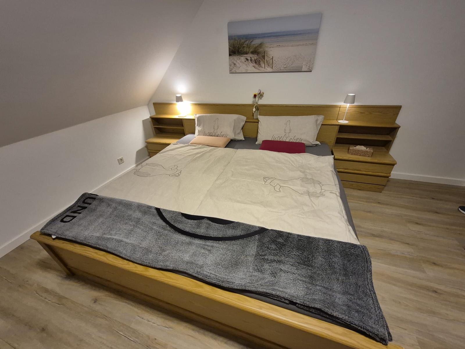 Schlafzimmer mit Holzbett, Nachttischen und Wandbild