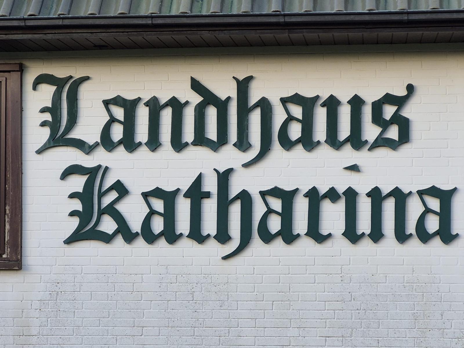 Schild Landhaus Katharina an weißer Ziegelwand unter Dach