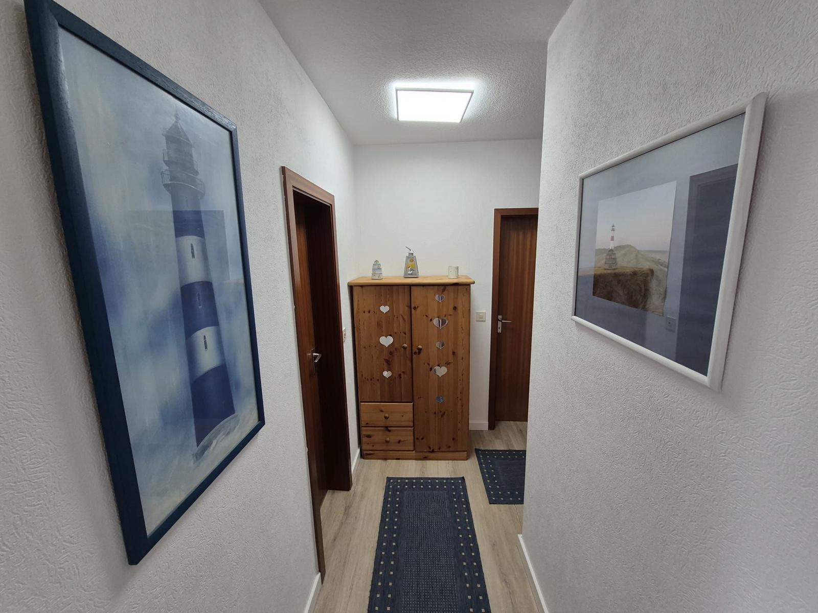 Flur mit Holzschrank, zwei Bildern an den Wänden und zwei Türen.