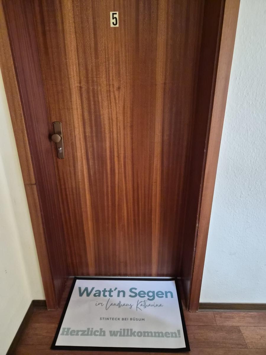 Holztür mit Nummer 5 und Willkommensmatte vor Eingang.