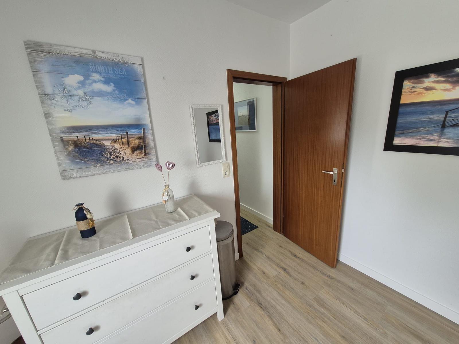 Eingangsbereich mit Schrank, Wandbildern und Tür zum Flur.