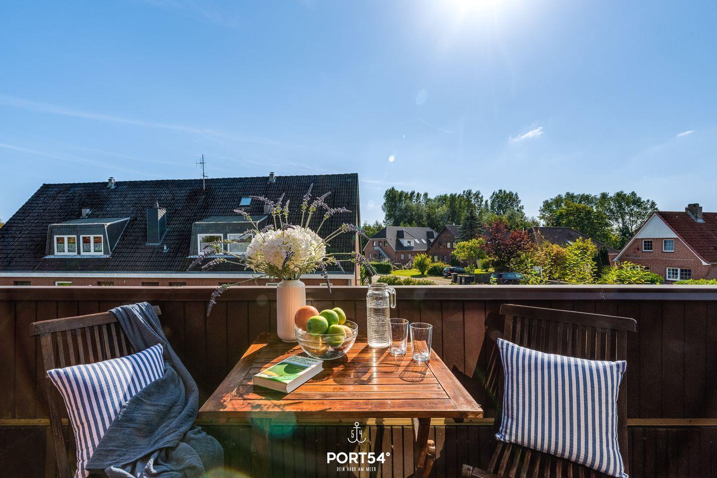 Terrasse mit Tisch, Stühlen und Blumen. Blick auf Häuser und Bäume unter blauem Himmel.
