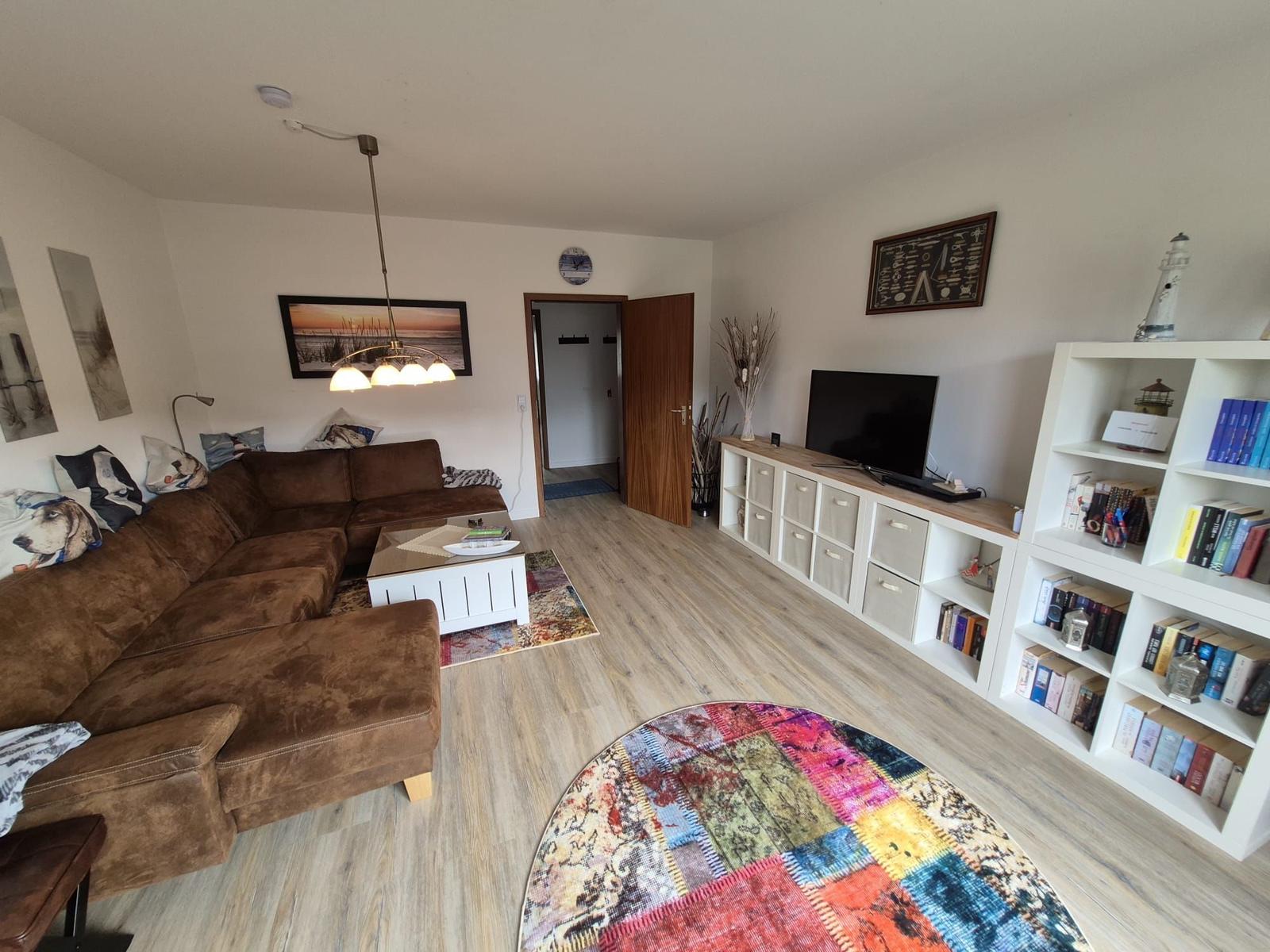 Wohnzimmer mit braunem Sofa, TV-Bereich und Bücherregal.