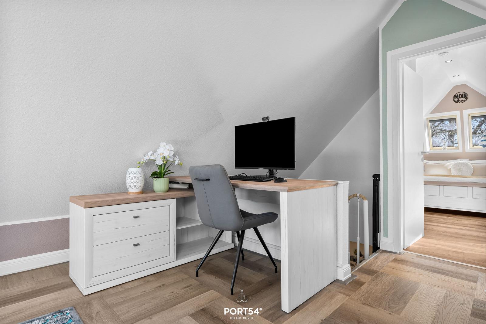 Arbeitsplatz mit Schreibtisch, Stuhl und Monitor unter schrägem Dach