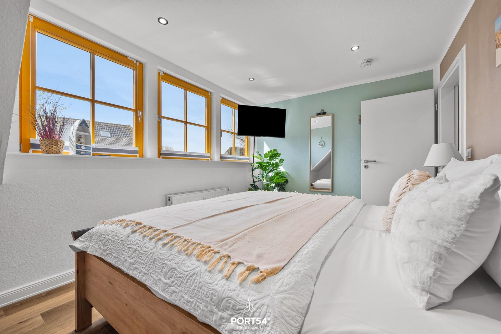Schlafzimmer mit Bett, Fenstern und Fernseher