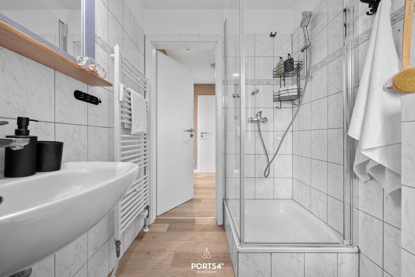 Badezimmer mit Dusche, Waschbecken und Heizkörper