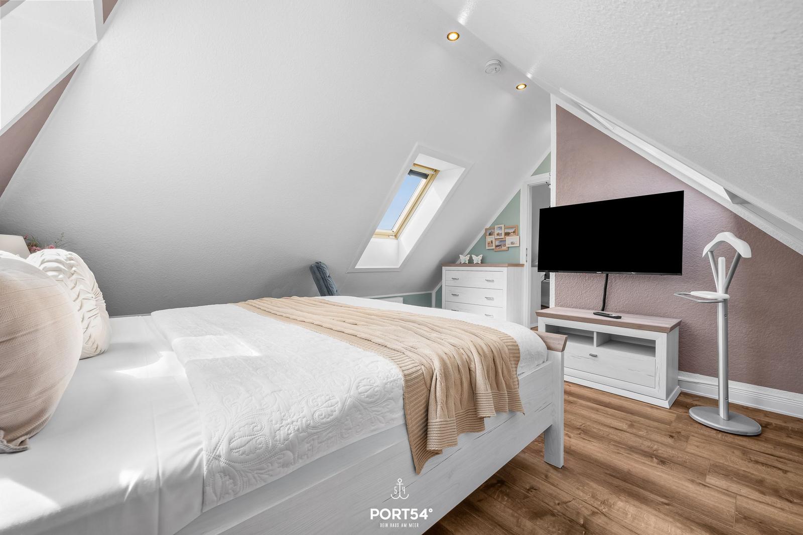 Schlafzimmer mit Dachfenster, Bett, Fernseher und Kleiderschrank.