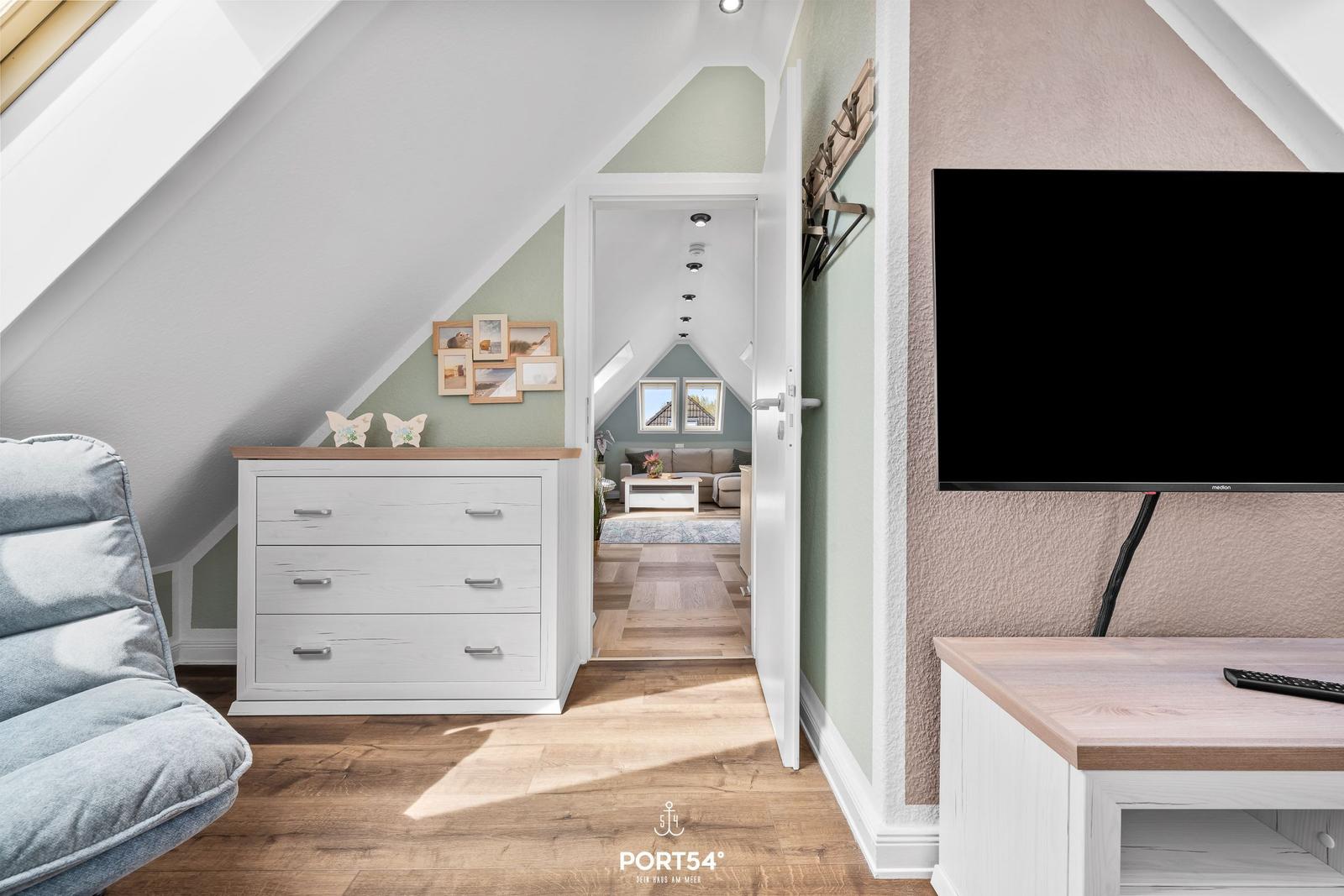 Schlafzimmer mit Schrank, Fernseher und Blick in Wohnbereich mit Sofa.