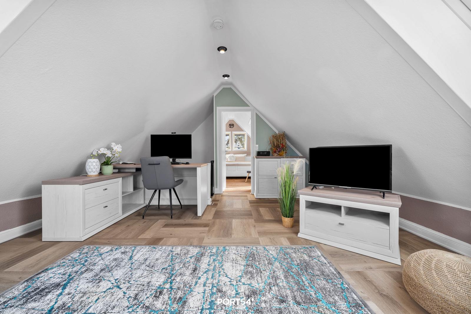 Ein Schlafzimmer mit Schreibtisch, Fernseher und Holzboden unter einem Dach