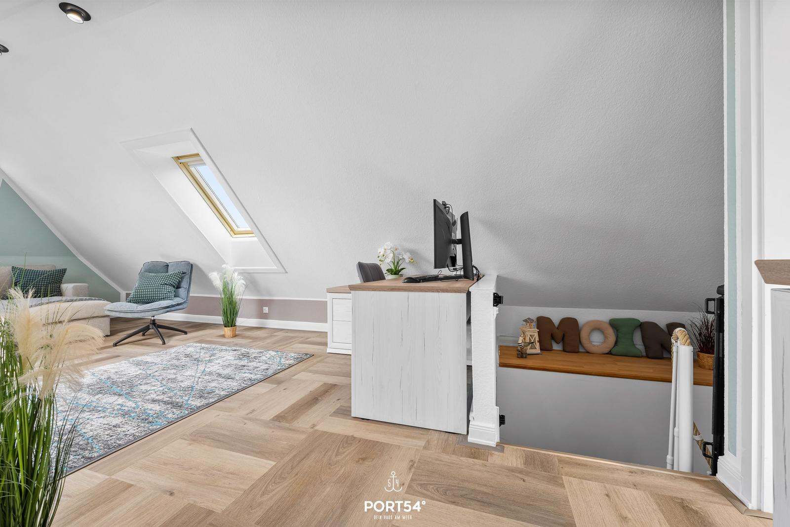 Dachgeschosszimmer mit Schreibtisch, Fenster und Sitzgelegenheit.