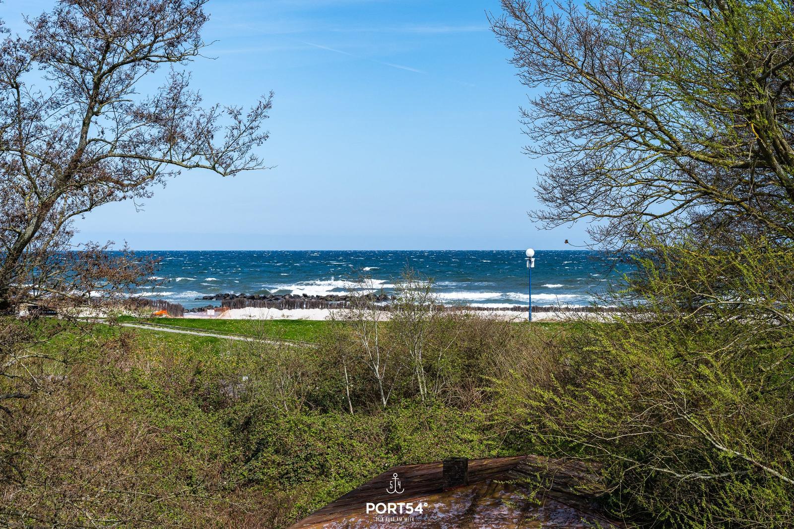 Meer mit Wellen, Strand und grüne Vegetation im Vordergrund.