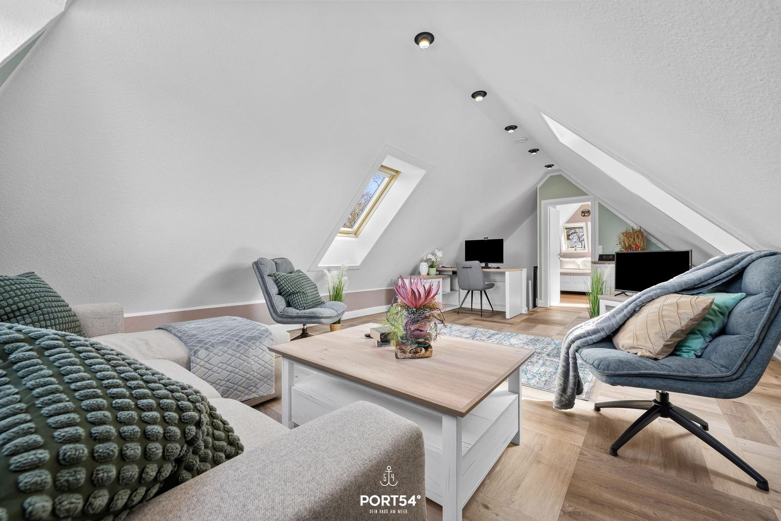 Wohnbereich mit Sofa, Sessel und Couchtisch unter Dachschrägen.