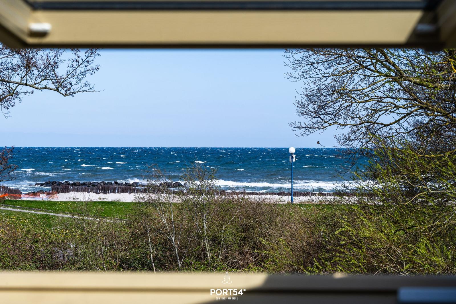 Meerblick von einem Fenster aus, mit Strand und Bäumen im Vordergrund.