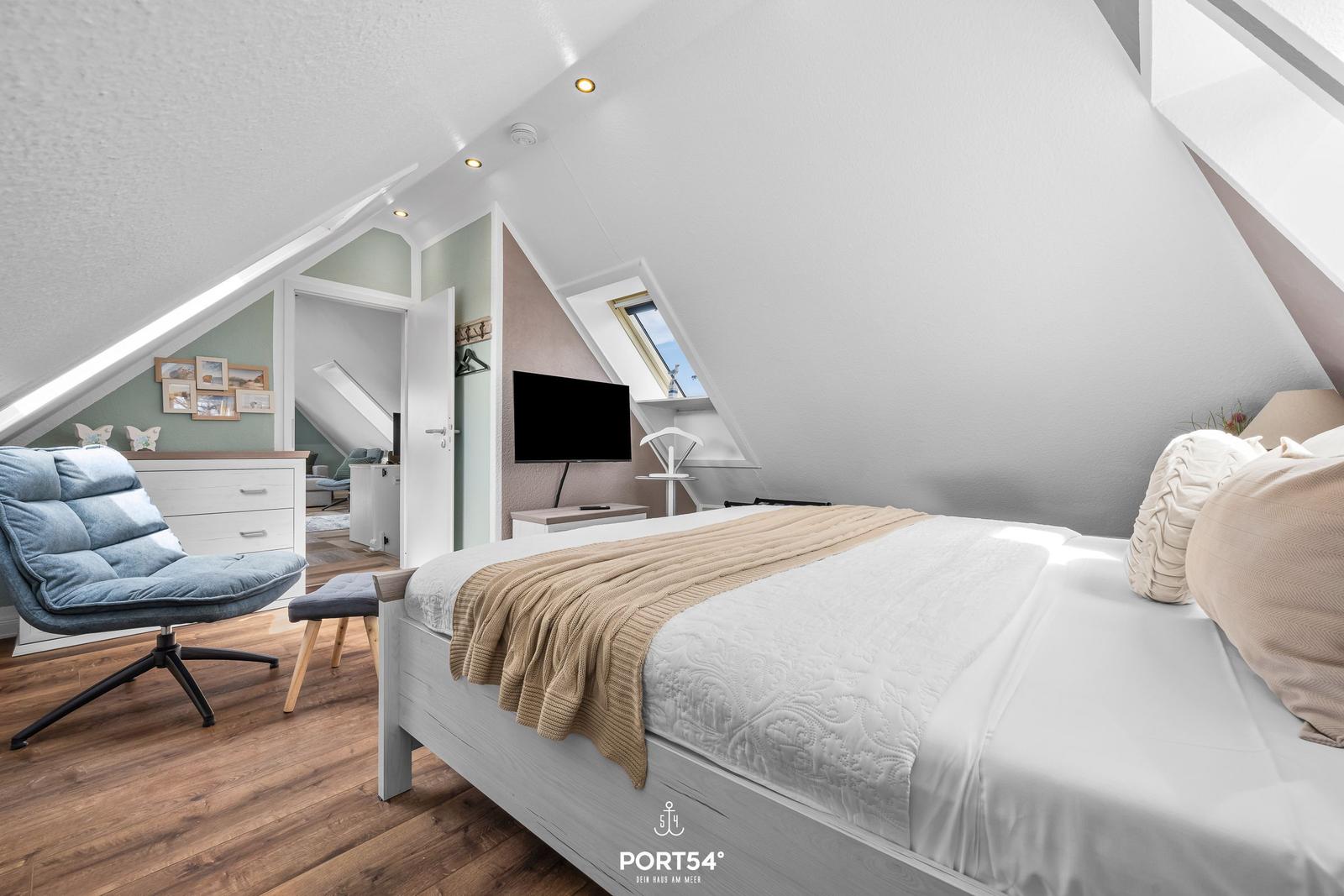 Schlafzimmer mit Dachschrägen, Bett, Fernseher und Sessel.
