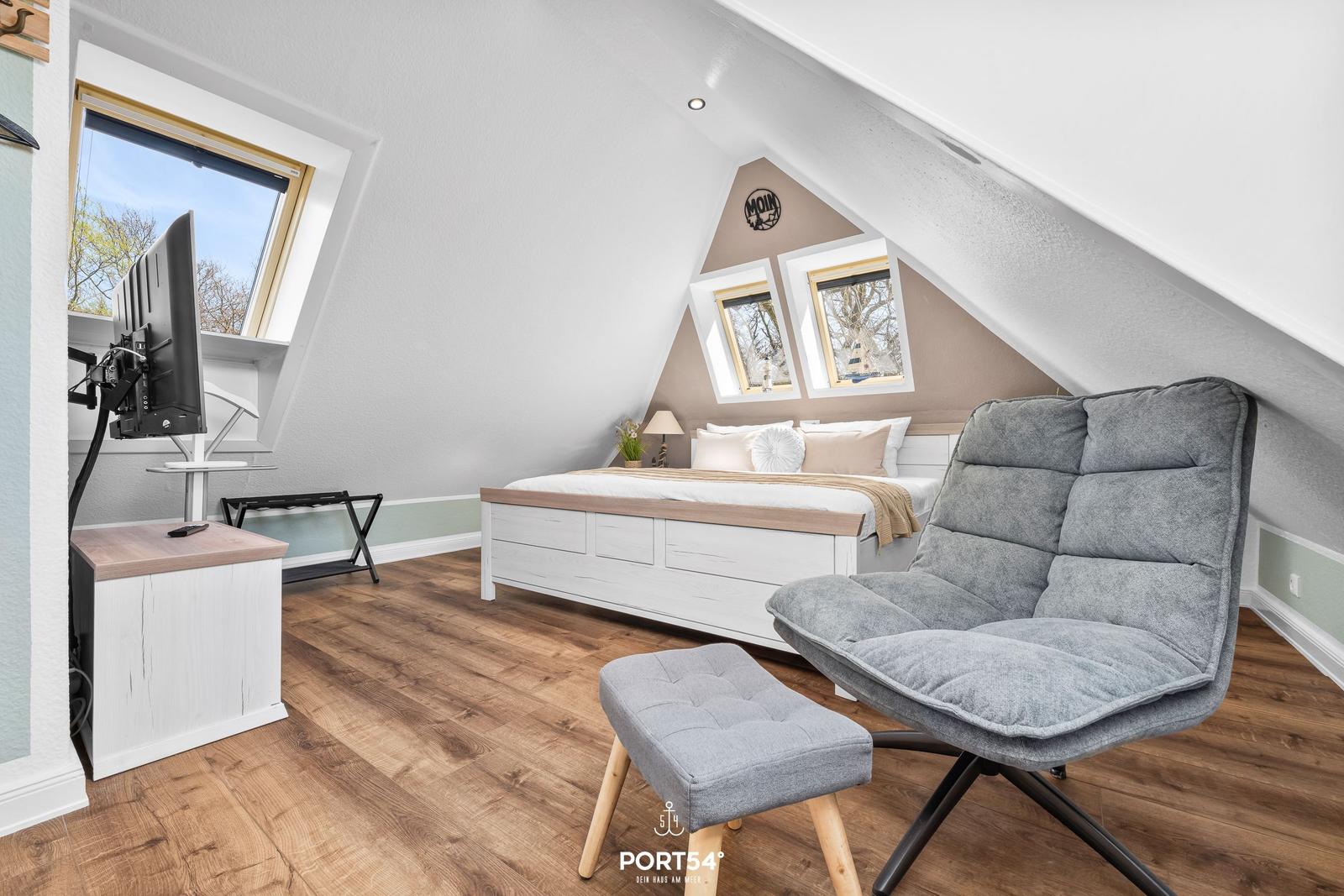 Schlafzimmer mit Dachschrägen, Bett, Sessel und TV.