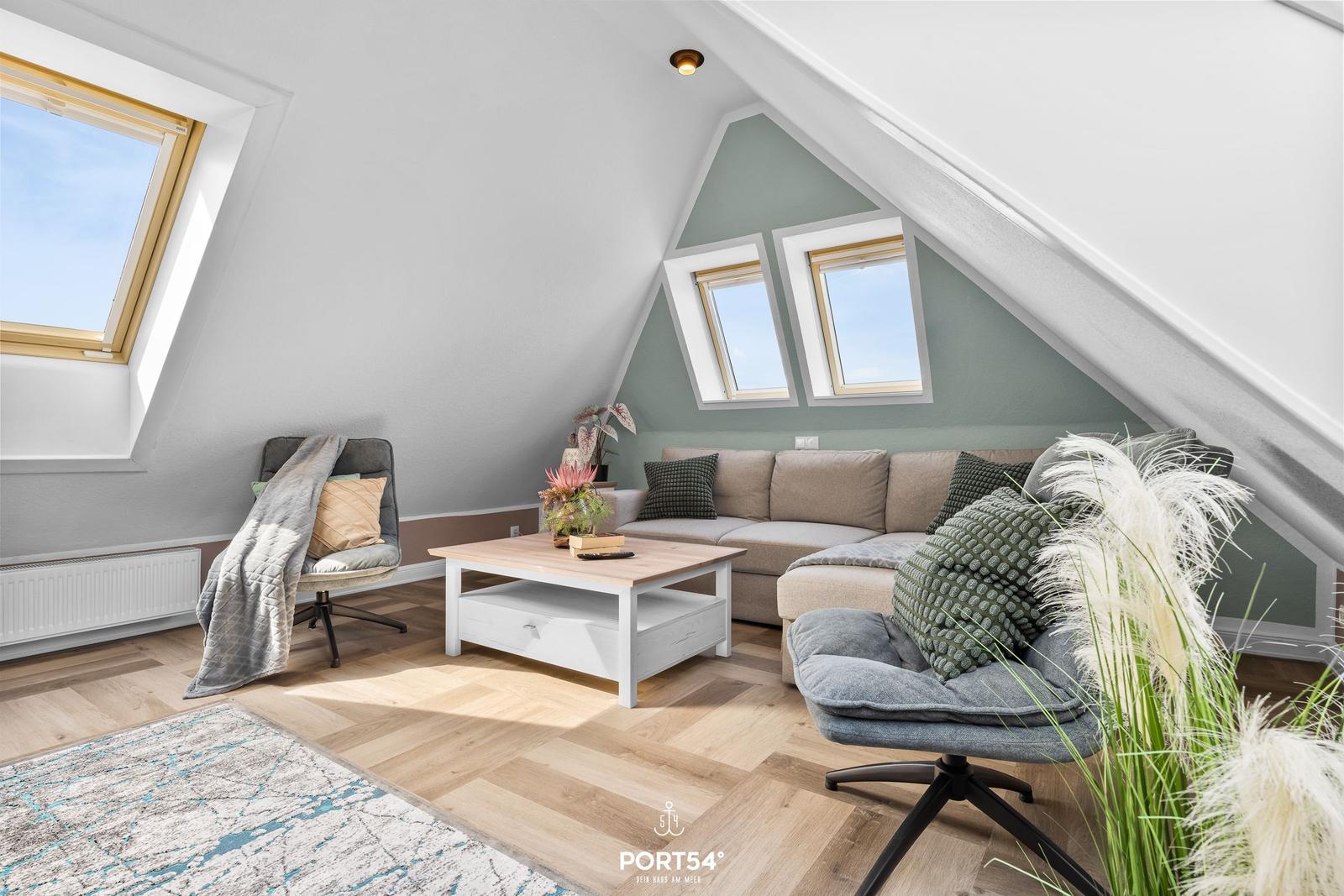 Wohnzimmer mit Sofa, Sessel und Tisch unter Dachschrägen mit Dachfenstern.