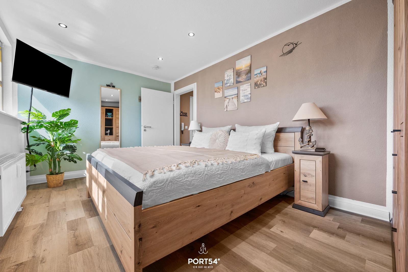 Schlafzimmer mit Holzbett, Nachttisch, Fernseher und Pflanze.