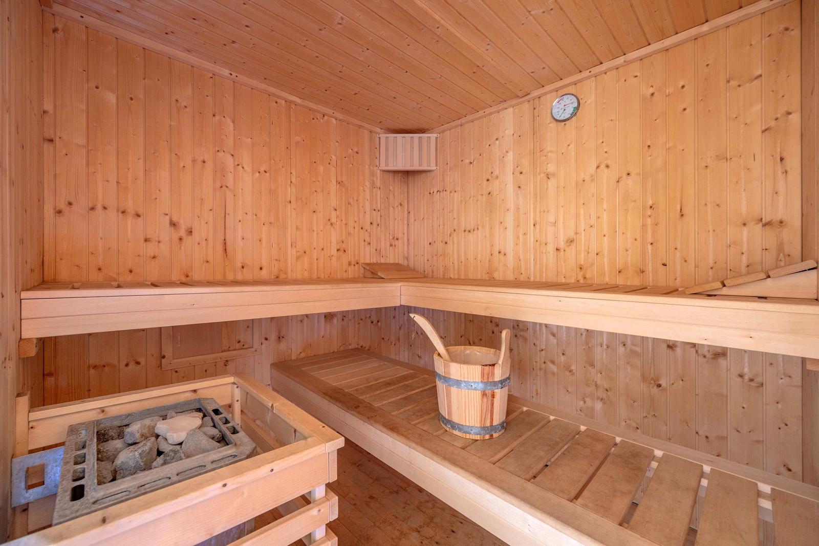 Sauna mit Holzbank, Steinofen und Holzbucket an der Wand.