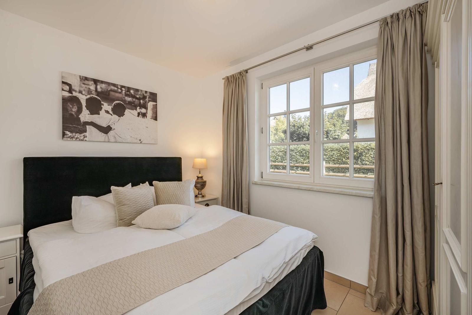 Schlafzimmer mit Bett, Fenster und Wandbild.