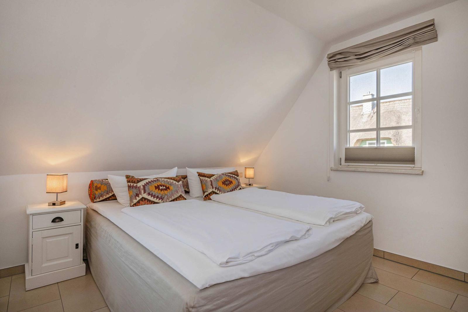 Ein Schlafzimmer mit Doppelbett, zwei Nachttischen und einem Fenster mit Blick auf Dächer.