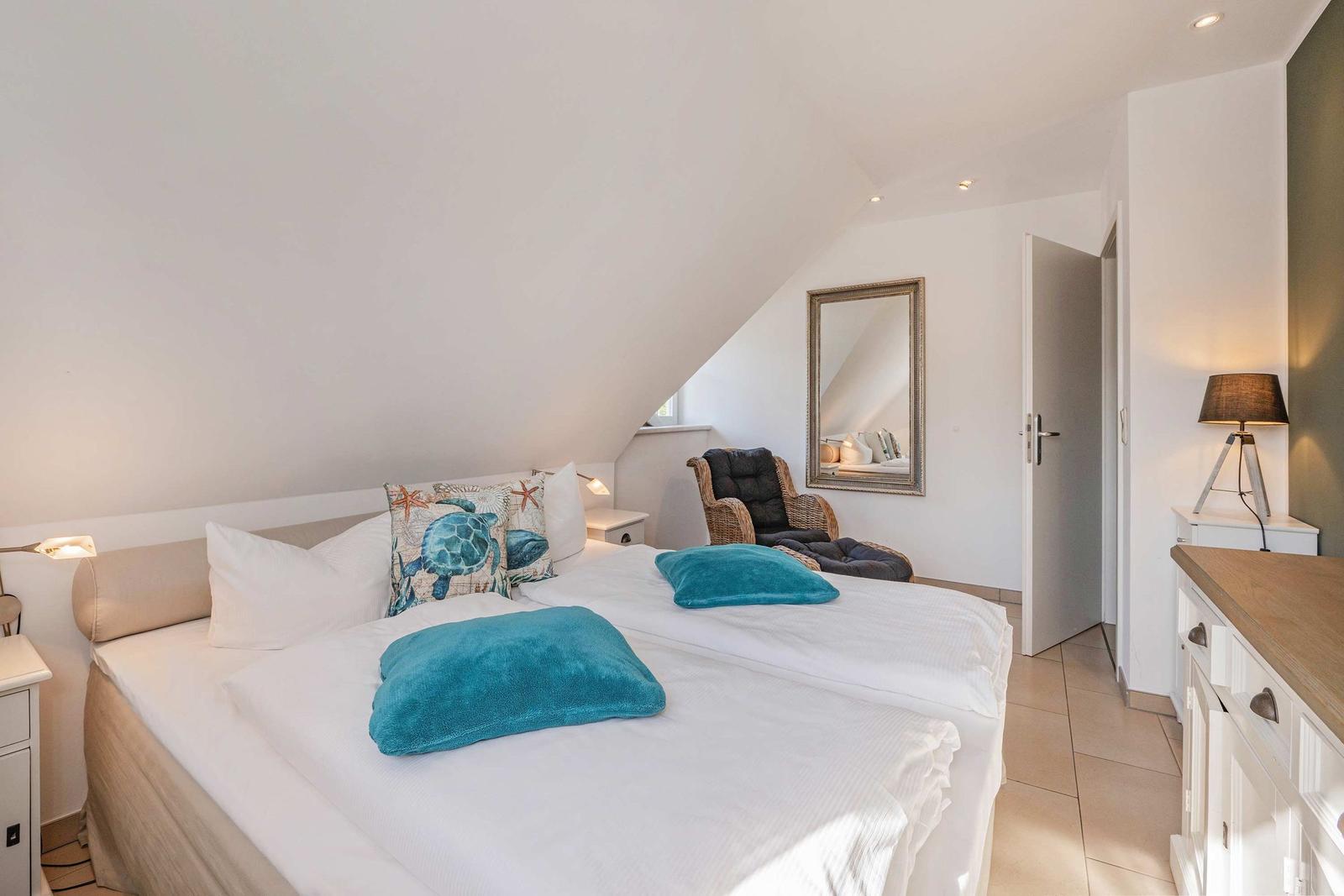 Schlafzimmer mit Doppelbett, blauen Kissen und Spiegel an der Wand.