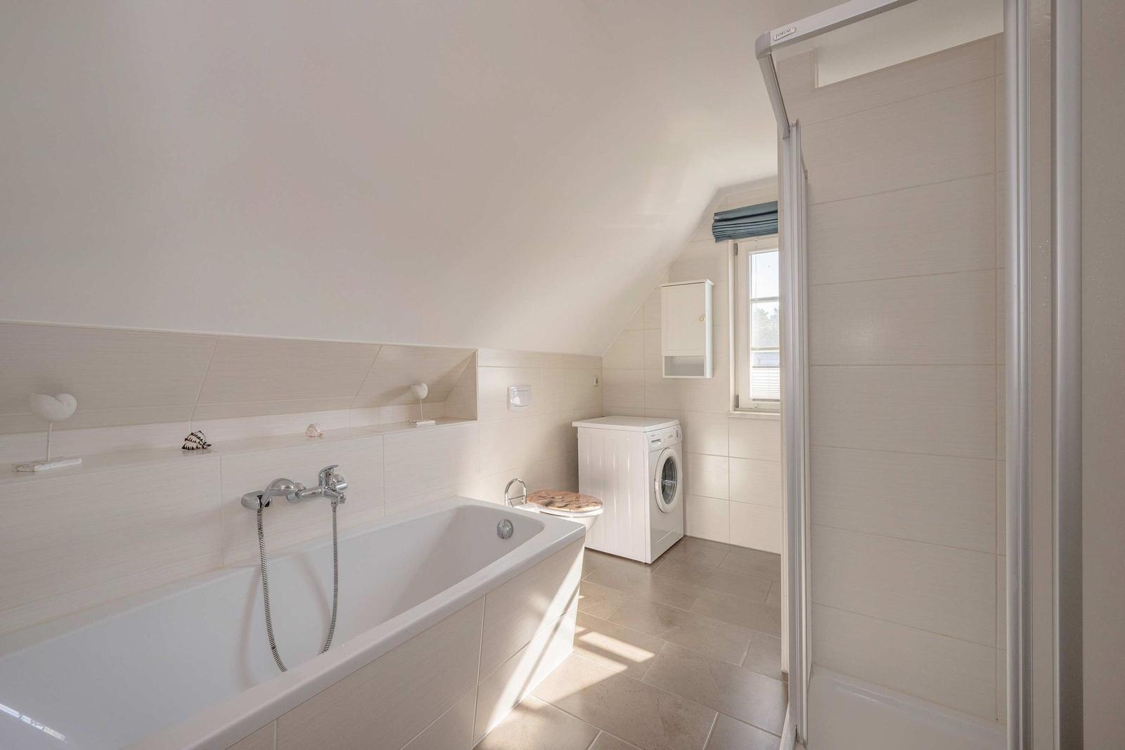 Badezimmer mit Badewanne, Waschmaschine und Dusche. Fenster mit blauem Rollladen.