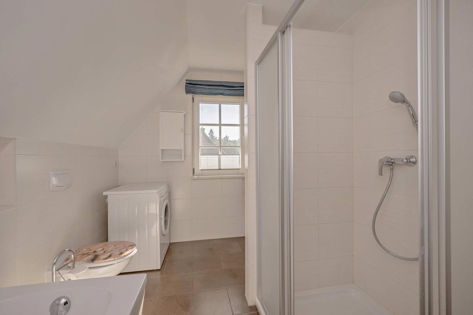 Badezimmer mit Dusche, Toilette und Waschmaschine unter Dachschrägen.
