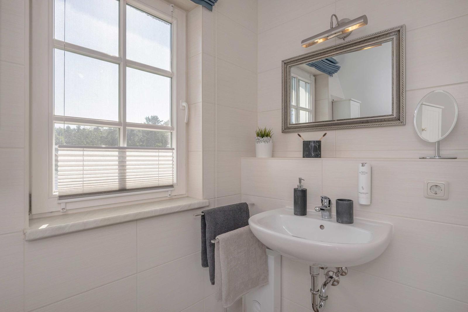 Badezimmer mit Waschbecken, Spiegel und Fenster mit Jalousie.