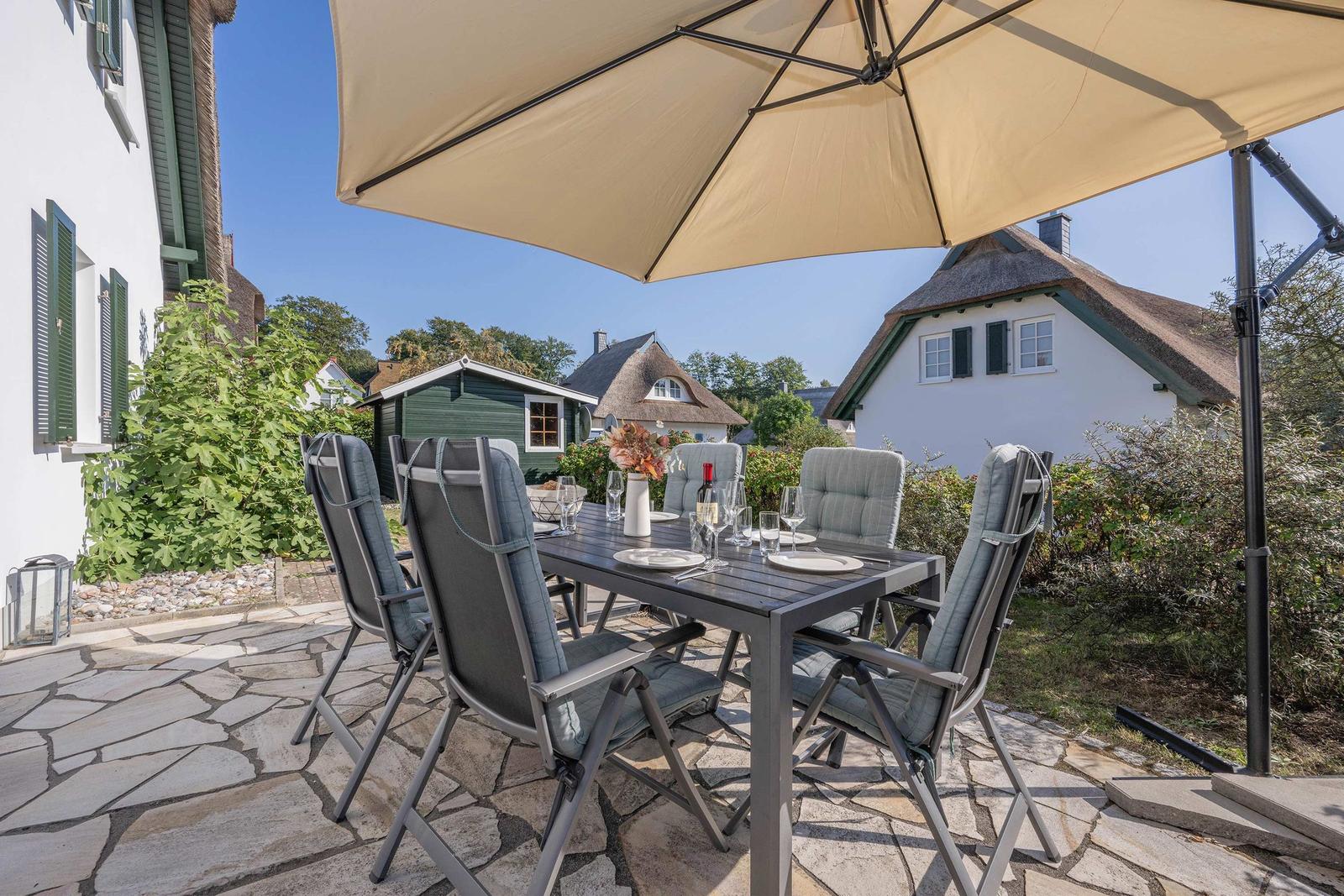 Terrasse mit Tisch, Stühlen und Sonnenschirm. Hintergrund: weiße Häuser mit Schindeldächern.