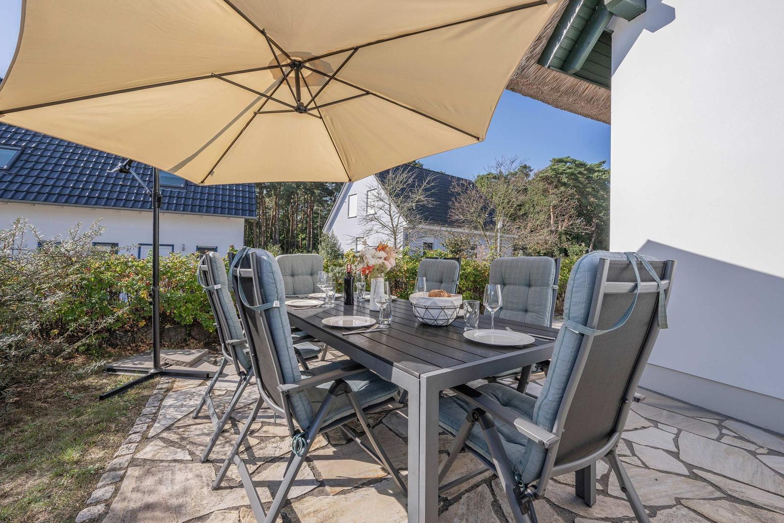 Terrasse mit gedecktem Tisch und Stühlen unter einem Sonnenschirm.