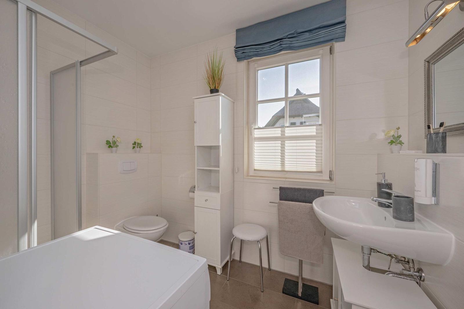 Badezimmer mit Dusche, Toilette, Waschbecken und Fenster mit Vorhang.