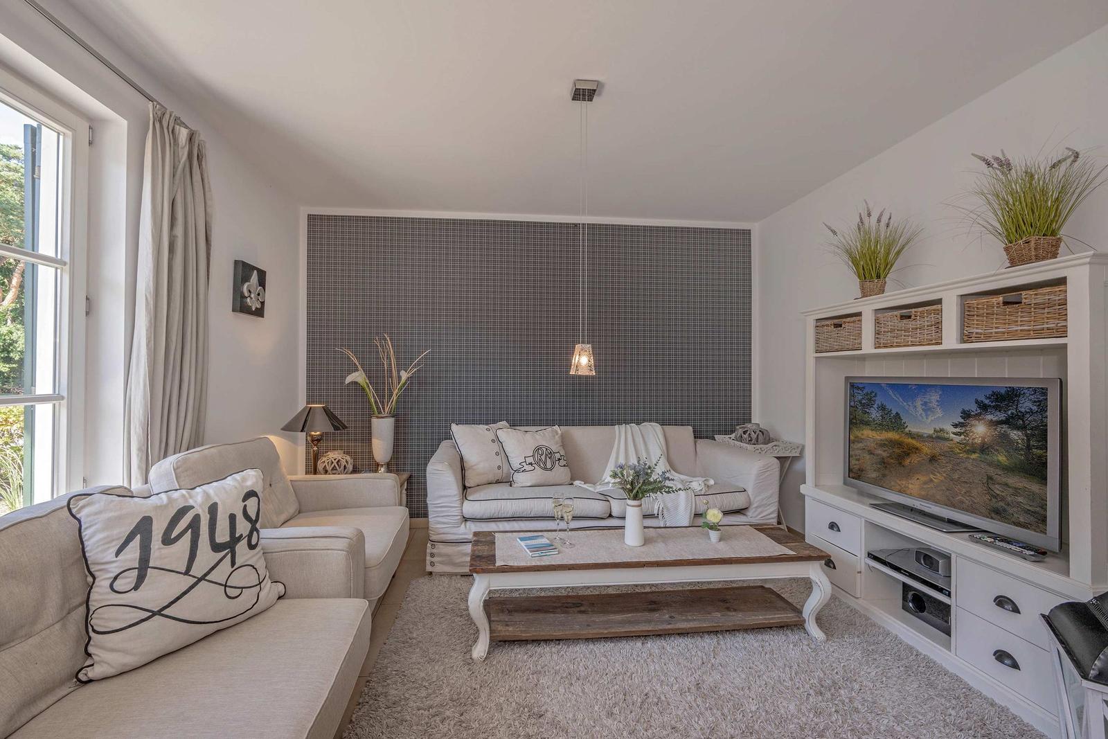 Wohnzimmer mit Sofa, Couchtisch und Fernsehregal. Wand mit Muster, Fenster mit Vorhang.